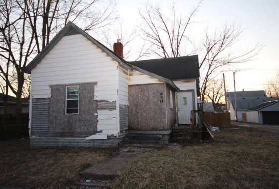 Abandoned house in disrepair with peeling paint and boarded-up windows at dusk