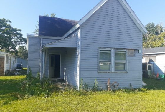 Weathered small blue house with overgrown yard under clear skies