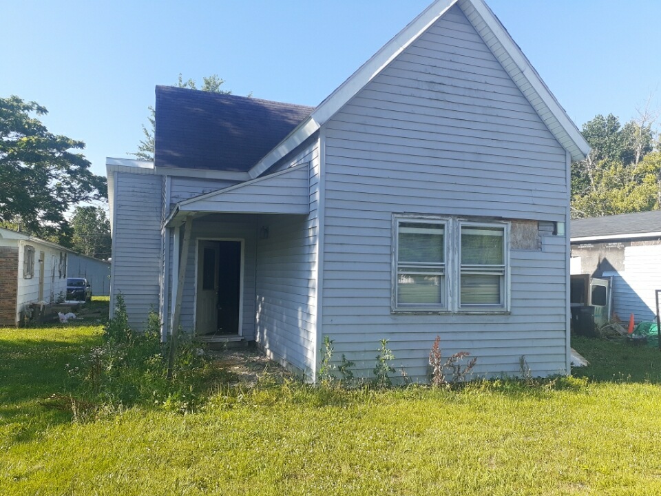 Weathered small blue house with overgrown yard under clear skies